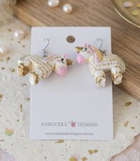 Unicorn pinata dangle earrings laid flat on Kaboodle Designs card among pearls and gold confetti