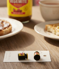 Close-up of two Vegemite jar earrings on a card, showing yellow lids and label detail against a wooden table