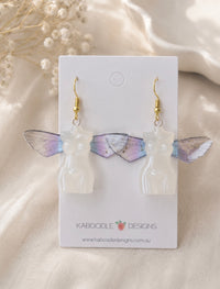 Pearly white resin torso earrings with iridescent lilac and blue butterfly wings on jewellery card