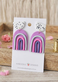 Purple clay rainbow drop earrings with speckled white top stud on Kaboodle card