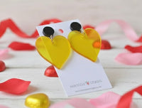 Yellow heart earrings on card surrounded by rose petals and foil-wrapped chocolate hearts