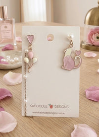 Mismatched pink cat and heart balloon enamel drop earrings displayed on card with pearl beads