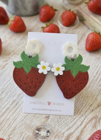 Glittery red acrylic strawberry drop earrings with white flower studs on branded card