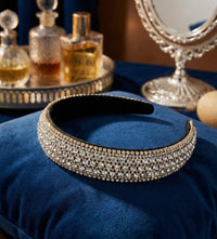 Rhinestone headband resting on blue velvet cushion beside a vanity mirror and perfume bottles