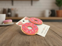 Close-up of pink donut earrings with sprinkles and glitter heart tops laid flat on a wooden table