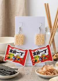 Instant noodle block and red ramen packet drop earrings on card, chopsticks in background
