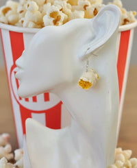 Close-up of a single popcorn earring worn on a model ear, showing buttery kernel detail