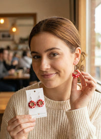 Woman wearing a red polkadot teacup earring while holding the matching card