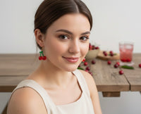 Woman wearing red cherry drop earring with green leaf detail, side profile
