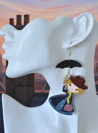 Close-up of nanny character earring worn on ear showing red glitter hat and blue glitter skirt detail