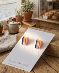 Rainbow layer cake stud earrings with black, blue, yellow and pink stripes on jewellery card