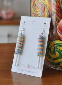 Close-up of rainbow candy earrings on card beside real swirl lollipops