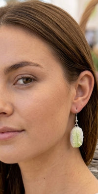 Close-up of model wearing a single green and white cabbage earring on her ear