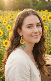 Sunflower and bee earring worn on model's ear in front of a sunflower field