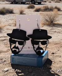 Black Perspex Heisenberg silhouette dangle earrings on card, shown against a desert backdrop