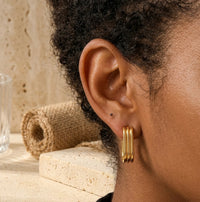 Close-up of ribbed gold hoop earring worn on ear, side view