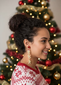 Woman wearing gingerbread man drop earrings with red glitter stud, side profile in front of Christmas tree