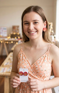 Woman wearing round red Sugus tin stud earrings, close-up on ears