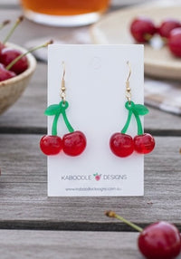 Cherry drop earrings on Kaboodle Designs card, red cherries with green stems and gold hooks