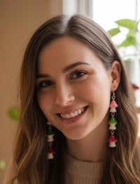 Close-up of woman wearing colourful mushroom drop earrings, showing pink, green and red charms against her hair