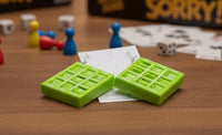 Pair of green noughts and crosses earrings lying on wooden table near dice and game pieces
