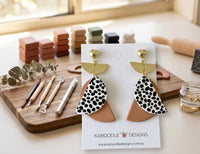 Clay geometric earrings on card displayed on workbench with clay blocks and sculpting tools