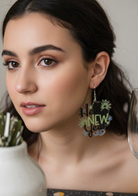 Close-up of woman wearing 'Hello New Year' drop earring, styled with champagne glass