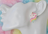 Close-up of a rainbow unicorn stud earring worn on an ear, showing pink, yellow and mint mane detail