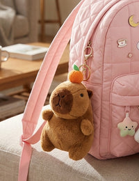 Brown capybara plush keychain with orange on head, clipped to pink quilted backpack strap