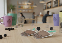 Pair of bubble tea earrings lying flat on wooden table with cafe setting in background