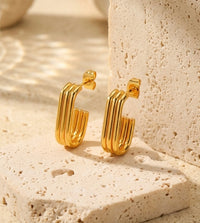 Ribbed gold-tone hoop earrings with squared J-shaped curve on stone surface