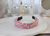 Pink striped knotted headband on white marble table with perfume bottles behind