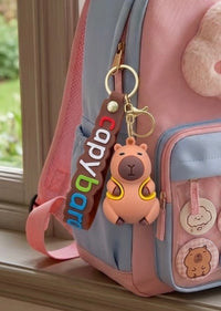 Close-up of tan capybara rubber keychain clipped to pastel backpack with colourful capybara word tag