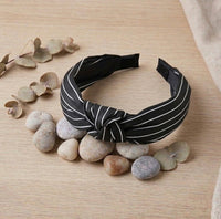 Black and white striped fabric knot headband on a wooden surface with pebbles and eucalyptus leaves