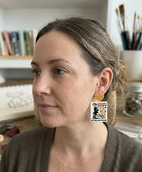 Close-up of crazy cat lady earring worn on ear, showing mustard top and printed cat illustration