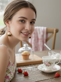Close-up of a woman wearing a strawberry cupcake earring, smiling at a tea table