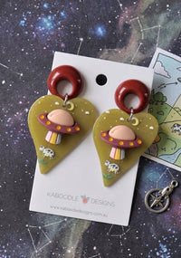 Acrylic UFO cow abduction drop earrings with burgundy ring hoop and mustard heart shape, shown on card