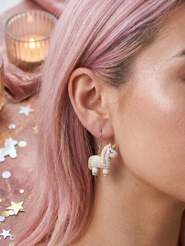 Close-up of unicorn pinata earring worn on ear, showing gold glitter mane and pink nose detail