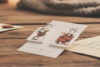 Joker and Queen card earrings laid flat on wooden table with playing cards