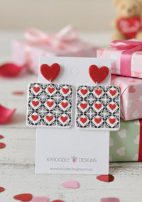 Red heart stud and black-and-white heart tile dangle earrings on Kaboodle Designs card, gift boxes behind