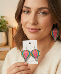 Close-up of woman wearing one striped hot air balloon drop earring reading 'explorer'