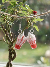 Strawberry milkshake earrings hanging outdoors on twine against green foliage background