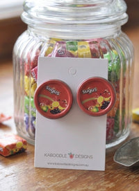 Round red Sugus tin drop earrings on a card, displayed against a jar of wrapped lollies