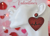 Close-up of red glitter heartbeat earring worn on ear against Valentine's backdrop