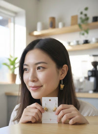 Woman wearing a bubble tea drop earring while holding the matching pair on its card