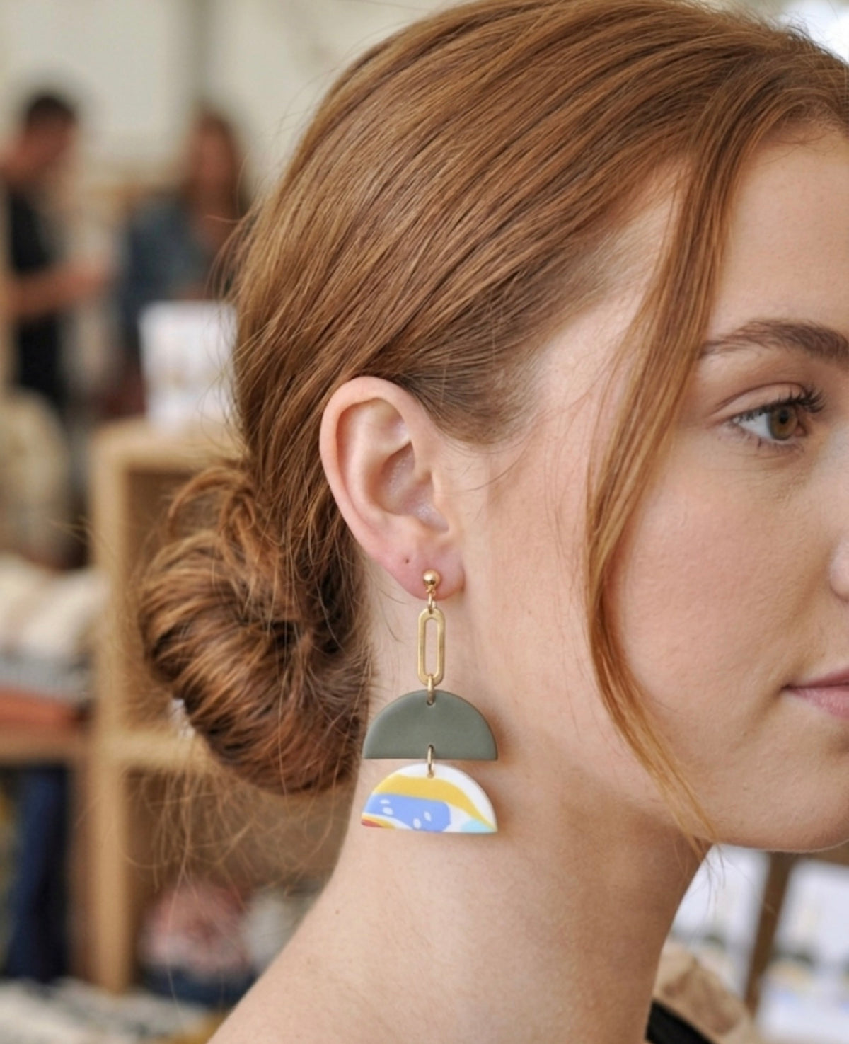 Close-up of geometric clay drop earring worn on ear showing gold stud and chain detail