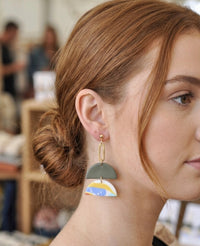 Close-up of geometric clay drop earring worn on ear showing gold stud and chain detail