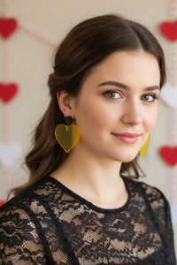 Close-up of woman wearing yellow heart drop earrings with black stud, styled with lace top