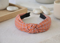 Burnt orange checkered knotted headband on linen surface, angled front view