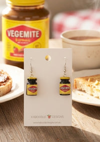 Pair of resin Vegemite jar earrings on a Kaboodle Designs card, with a real Vegemite jar and toast in the background